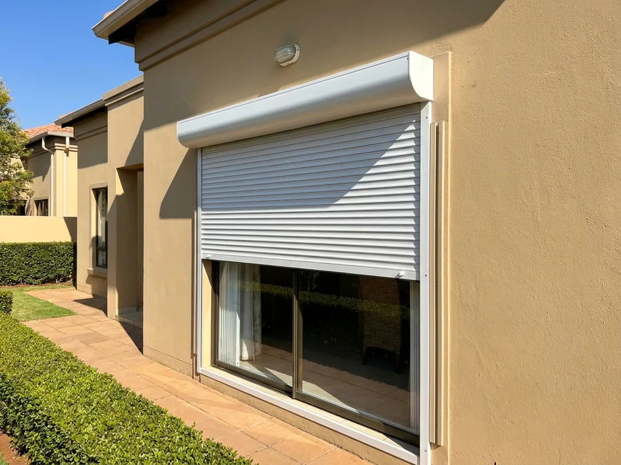 White aluminium roller shutter lowered two-thirds over a sliding patio door, riding in slim side channels beneath its rounded headbox